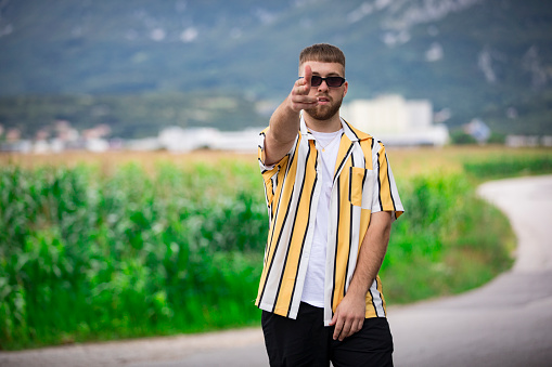 Portrait of Young Adult Man Pointing at Camera and Standing on Country Road.