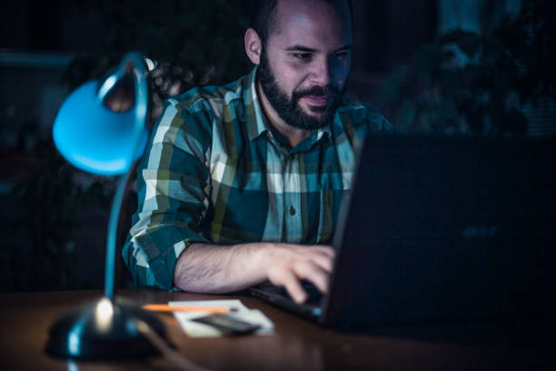 istock Man using a laptop and sitting at the desk at home late night 1264456748