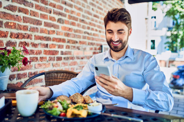istock Smiling young businessman using smartphone and eating breakfast in outdoors cafe 1264457314
