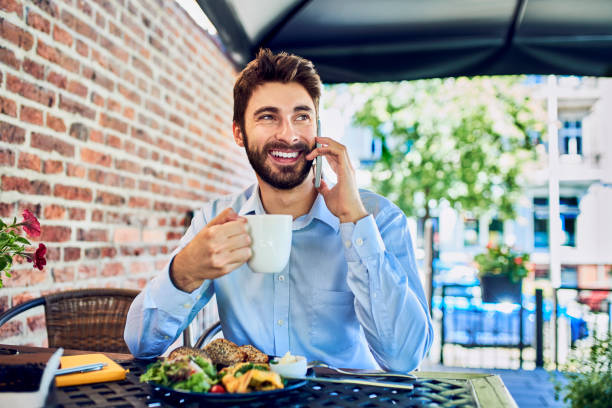 istock Young businessman talking on phone while eating breakfast in outdoors cafe 1264457450