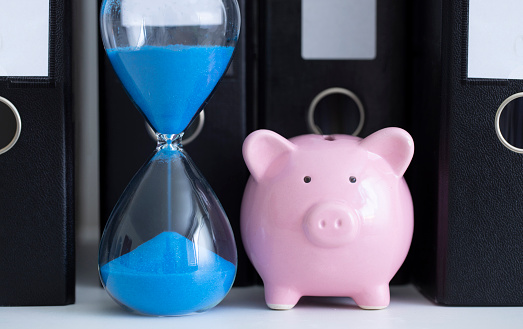 Blue hourglass and a piggy bank in front of a row of office folders