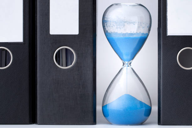 istock Blue hourglass, half expired, stands between a row of files 1264458672