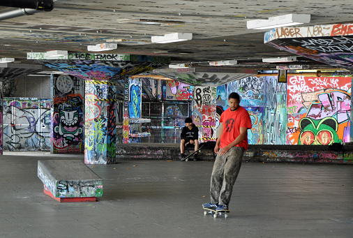 Public concrete graffiti covered skateboard / BMX park with skaters including a young black male on a skateboard. Under the Royal Festival Hall. River Thames Southbank. Outdoors on a summers day. London, United Kingdom, August 2, 2020