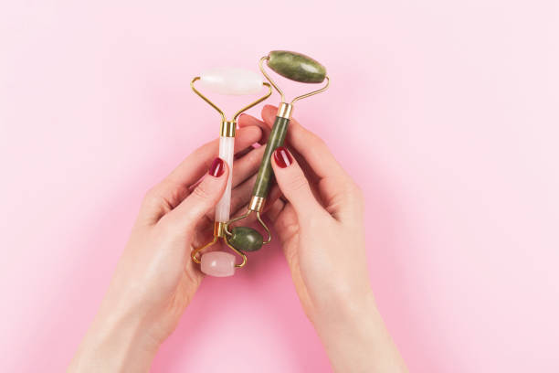istock Two jade rollers in woman hands on pink background. 1264463022