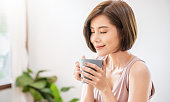 白い寝室でコーヒーカップ朝の春の時間を保持している若い美しいアジアの女性の手の肖像画。夏に楽しくリラックス。韓国メイクウェイクアップ大学アジアライフスタイルコンセプト。
