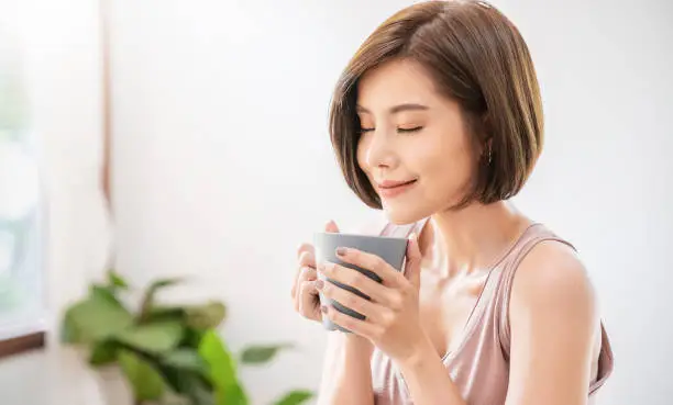 Portrait of young beautiful asian woman hands holding coffee cup morning spring time in white bedroom. Happy cheerful relaxing in summer. Korean makeup wakeup university asia lifestyle concept.