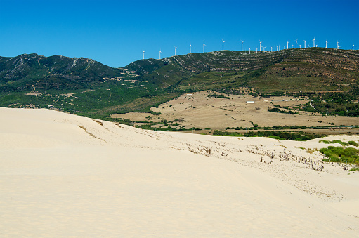 Sand dune and green mountains with windmills on the background. Punta Paloma beach. Tarifa, province of Cadiz, Spain.