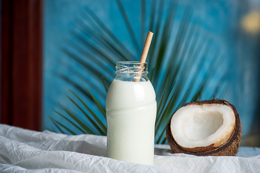 Coconut milk with halved fresh coconut on a table with copy space