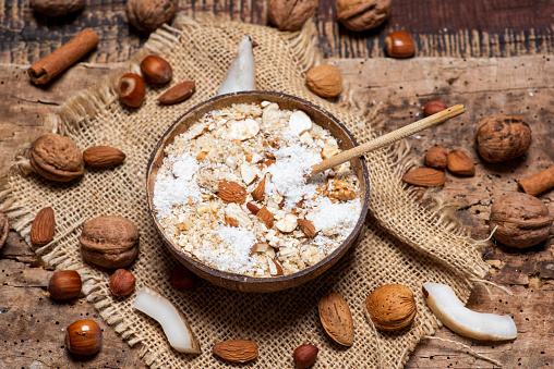 Oatmeal cereals with grated coconut and nuts in a bowl of coconut shell tabletop view