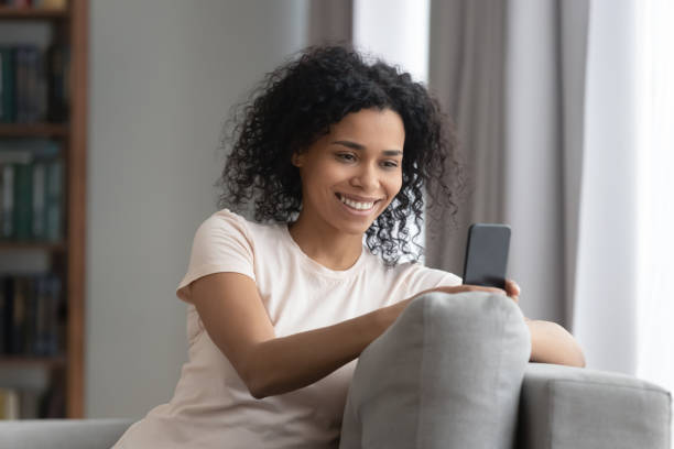 istock Smiling African American woman using cellphone, relaxing on couch 1264479249