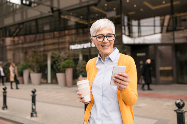 istock Smiling Caucasian senior woman using a smart phone and drinking coffee 1264479809
