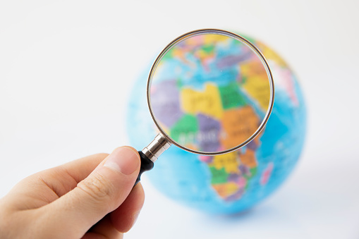 Man holding magnifying glass to world globe