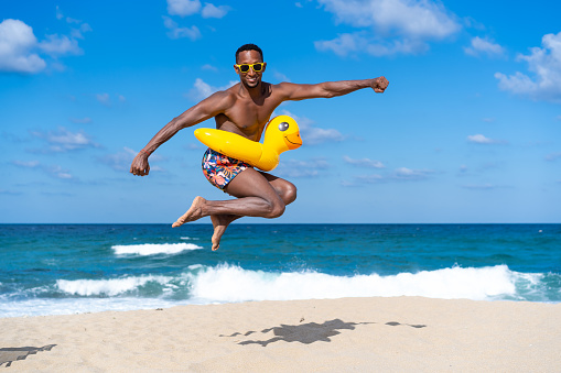 Afro men wearing inflatable ring and jumping on the beach