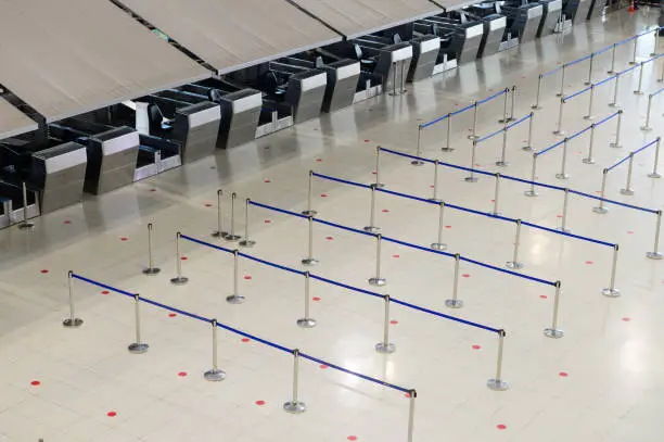 Empty airport check-in counter hall with crowd control barriers.