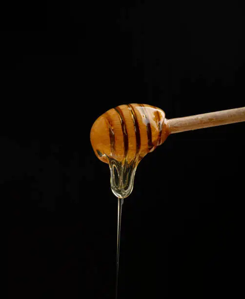 Photo of Close up honey flowing from wooden dipper on black