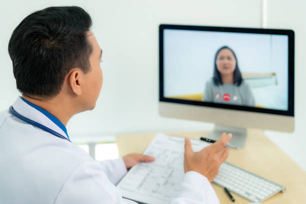 istock Asian man doctor wears white coat and headset speaking videoconferencing on laptop computer using online video call consultation app. Remote medical help for distance patient, telemedicine. 1264492608