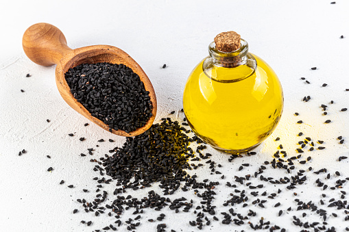 Black cumin oil with seeds on wooden background. glass bottle of black cumin seeds essential oil , Nigella Sativa in spoon and bowl on wooden rustic background.