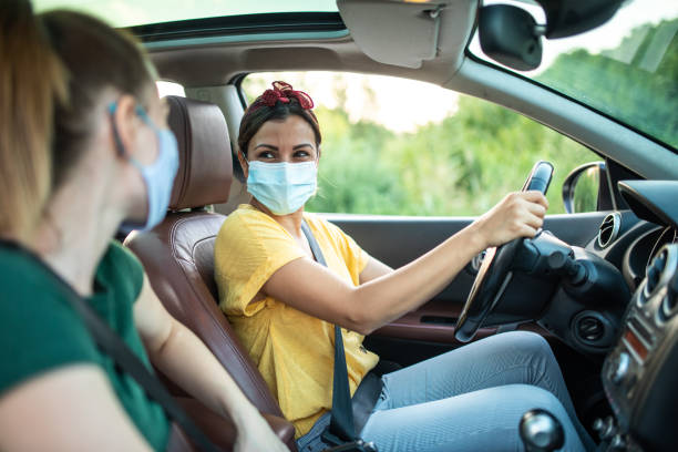 Smiling friends with protective face masks in ride sharing car Two smiling female friends with protective face masks, talking and enjoying a ride together in ride sharing car car pooling photos stock pictures, royalty-free photos & images
