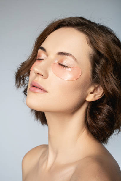 Serene young woman with perfect skin using under-eye patches