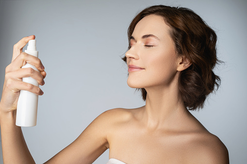 Close up of attractive lady with perfect skin using cosmetic product while standing against blue background