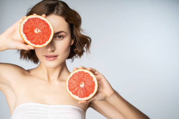 attractive young woman with perfect skin holding grapefruit halves - facial expression isolated lifestyles exoticism imagens e fotografias de stock