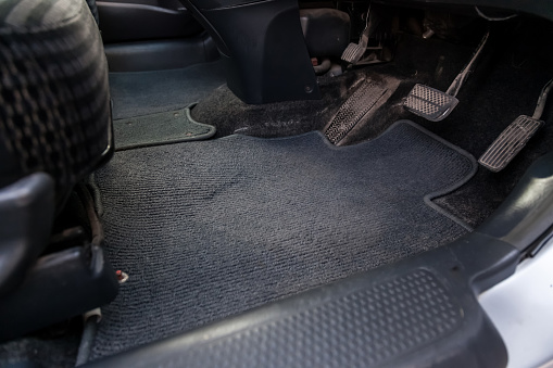 Dirty car rug made of dark blue fabric material with gas, brake and clutch pedals in a auto service before dry cleaning.