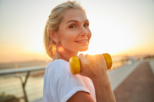 Portrait of a good-looking cheerful middle-aged athletic woman with a dumbbell posing for the camera