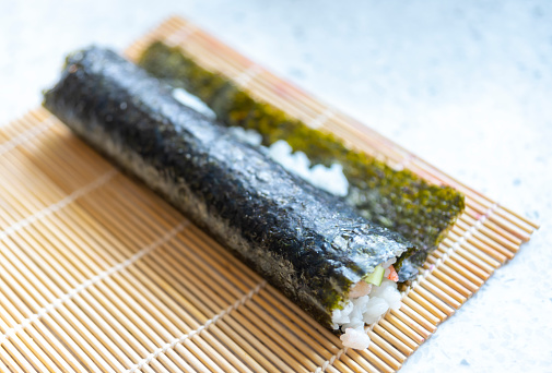Preparing homemade Sushi.  This shows a sushi roll before being cut into bite size portions.