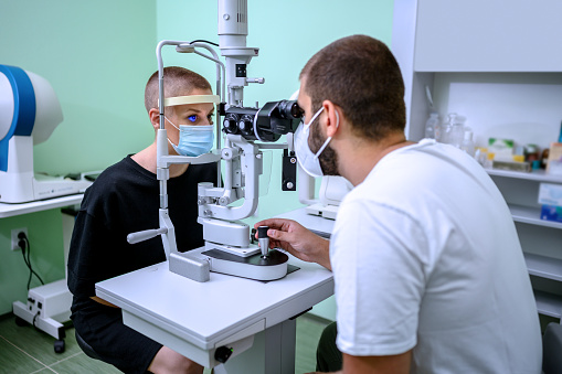 Male ophthalmologist examining woman's eyesight with optical instrument. Male ophthalmologist measuring an eyesight of a woman with diagnostic medical tool.