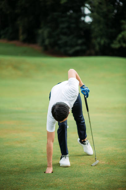 asiatische chinesische junge männliche golfer abholen golfball am loch des golfplatzes - golf golf course putting green hole stock-fotos und bilder