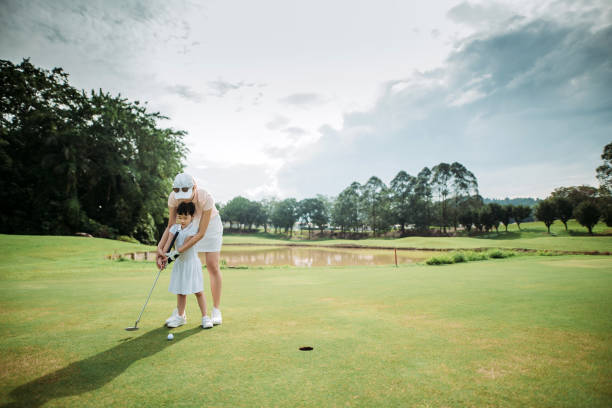 jovem golfista chinesa asiática ensinando sua filha a jogar golfe no campo de golfe - golf women female concentration - fotografias e filmes do acervo