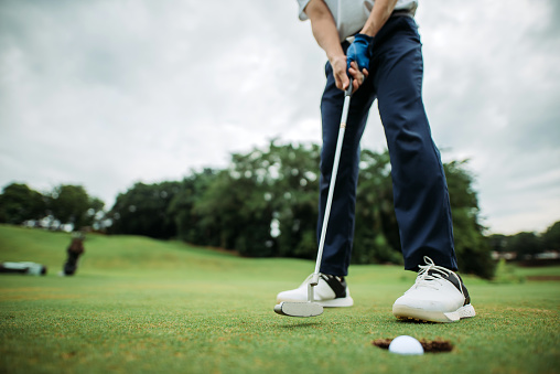 Disparo de cosecha de asiático chino joven golfista masculino tocando la pelota de golf en un agujero en el campo de golf photo