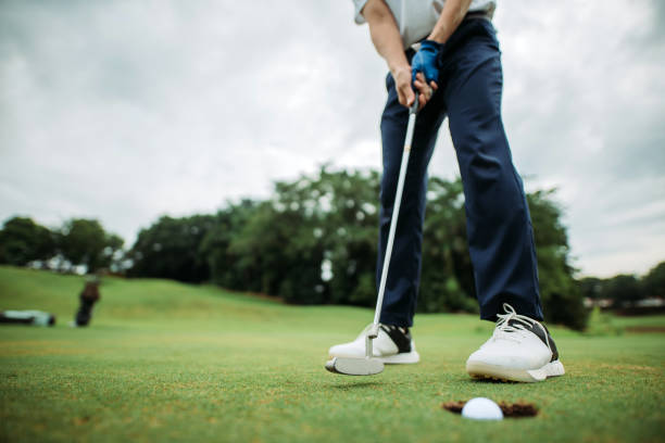 coup de culture du jeune golfeur mâle chinois asiatique tapant la bille de golf dans un trou au terrain de golf - golf playing men ball photos et images de collection