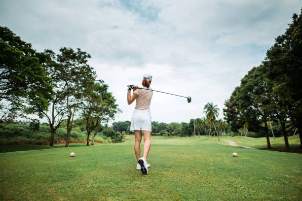 Rear view of asian chinese young female golfer teeing off and swing her driver club on the golf course stock photo