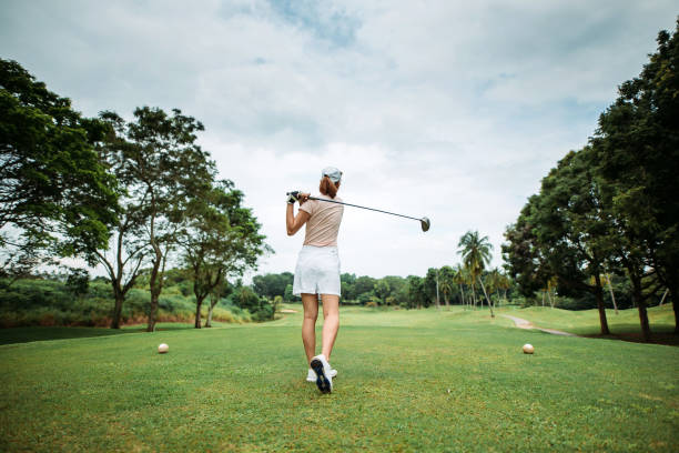 Rear view of asian chinese young female golfer teeing off and swing her driver club on the golf course relax and enjoying a day, full length of view golf concentration stock pictures, royalty-free photos & images