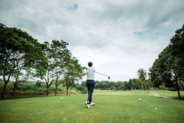 rear view of asian chinese young male golfer teeing off and swing his driver club on the golf course - golf golf swing putting cheerful imagens e fotografias de stock