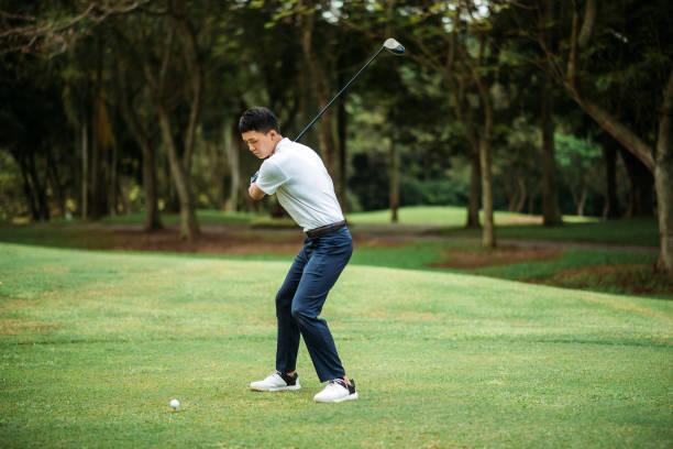 азиатский китайский молодой мужчина игрок в гольф teeing покинуть и качели его водитель клуб на поле для гольфа - golf golf swing putting cheerful стоковые фото и изображения