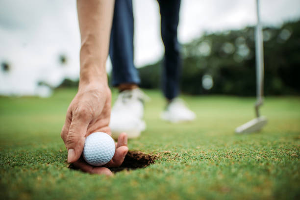 primer plano de asiático chino joven golfista masculino recogiendo pelota de golf con la mano en el hoyo del campo de golf - golf expertise professional sport men fotografías e imágenes de stock