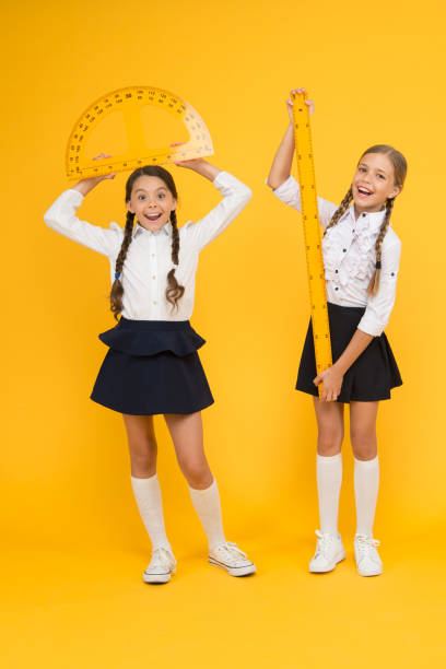 istock Formula. back to school. Maths and geometry. Kids in uniform at yellow wall. friendship and sisterhood. happy small girls study mathematics. students use protractor ruler. stem disciplines 1264529446