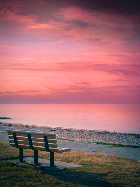 tranquil pink twilight seascape and dramatic cloudscape over the bench on cape cod beach - beach bench cape cod sunset imagens e fotografias de stock