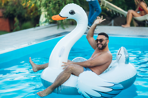 Young caucasian handsome carefree man on float swan enjoying in swimming pool.