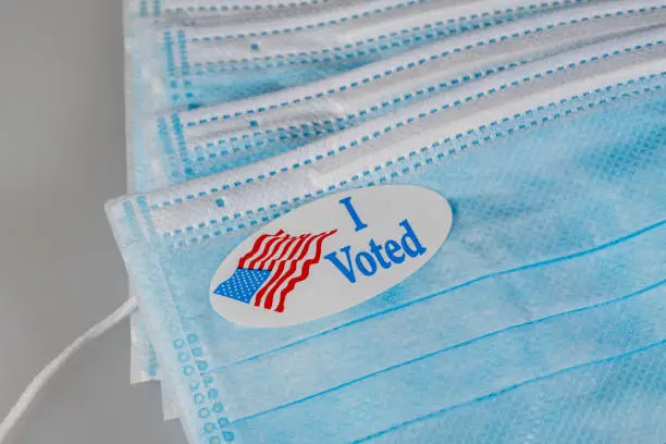 Photo of I Voted paper sticker on medical face mask to illustrate in person voting