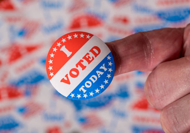 istock Finger with I Voted Today sticker in front of background created from many election voting badges 1264536715