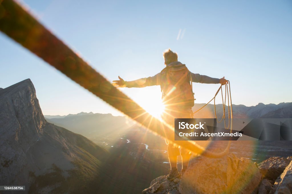 Mountaineer spreads arms to celebrate on mountain summit At sunrise; mountain range distant Motivation Stock Photo