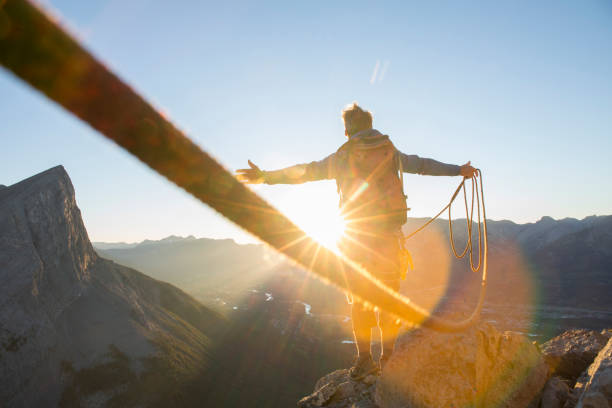 Mountaineer spreads arms to celebrate on mountain summit At sunrise; mountain range distant rocky mountains north america stock pictures, royalty-free photos & images