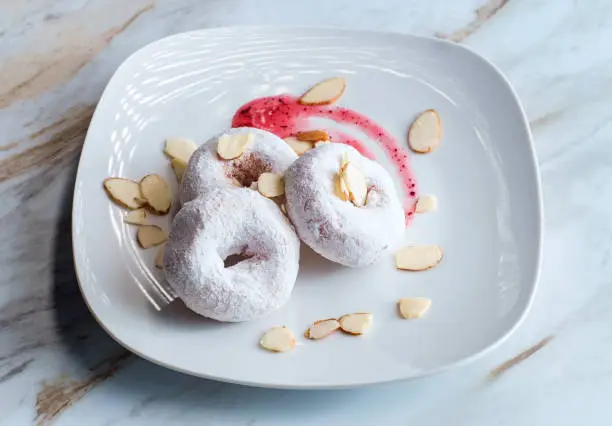 Powdered sugar cake doughnuts with holes served with raspberry jam and slivered almonds
