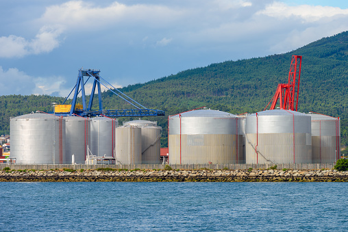 industrial fuel tanks in the seaport against the backdrop of mountains covered with green forest