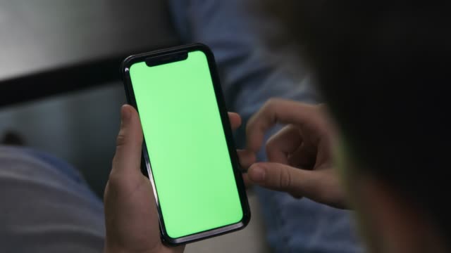 Young male holding cellphone swiping and scrolling green screen