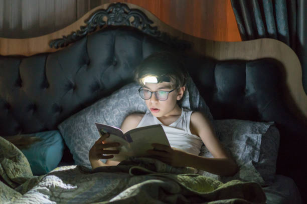 istock Young boy reading a book on the bed with flashlight 1264555715