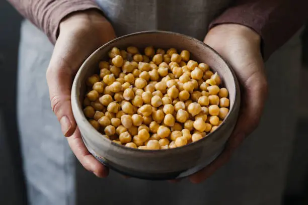 Healthy food: unrecognizable woman holding chickpeas in a clay bowl.